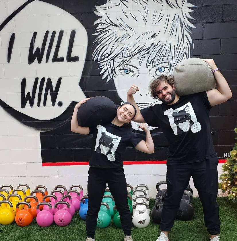 Two women flexing in front of “I Will Win” mural